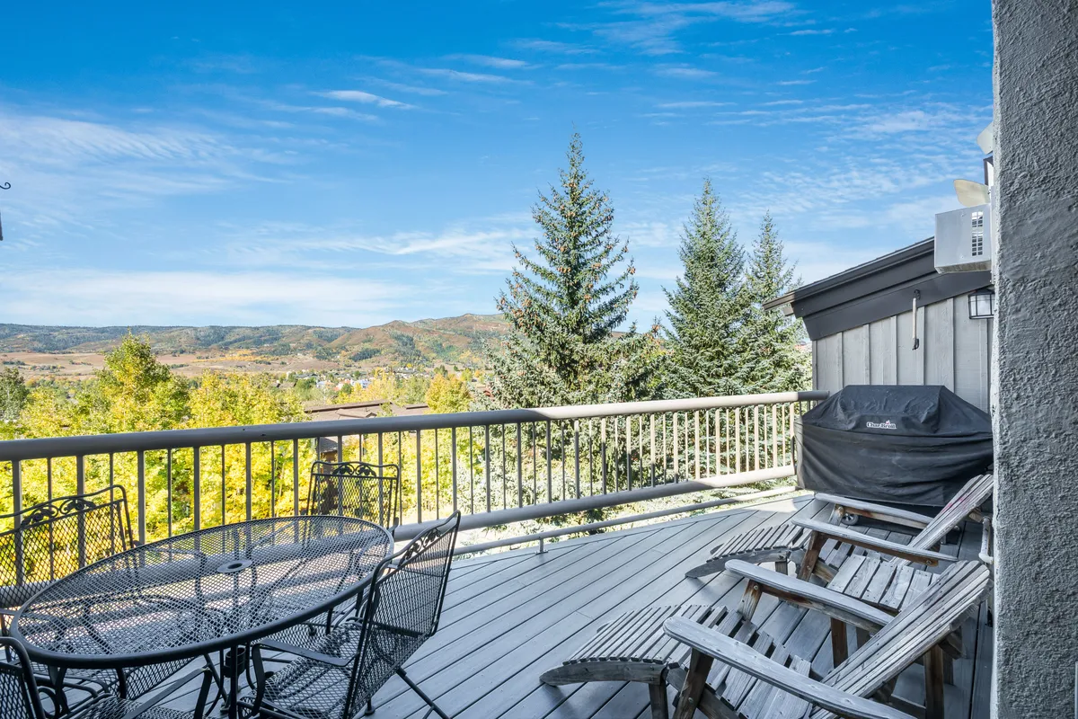 An inviting outdoor dining area with a grill and plenty of seating, set against a scenic backdrop of mountains and trees. The space is ideal for unwinding after a day of adventure or sharing stories with friends in the fresh mountain air. The combination of amenities and views makes it appealing year-round.