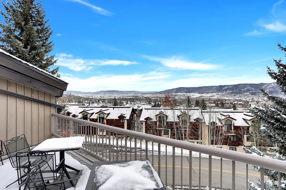 A balcony with seating overlooks snow-covered rooftops and a distant mountain range, inviting guests to enjoy morning coffee or sunsets in the fresh alpine air. The outdoor space is intimate, yet offers expansive valley and Flat Tops views.