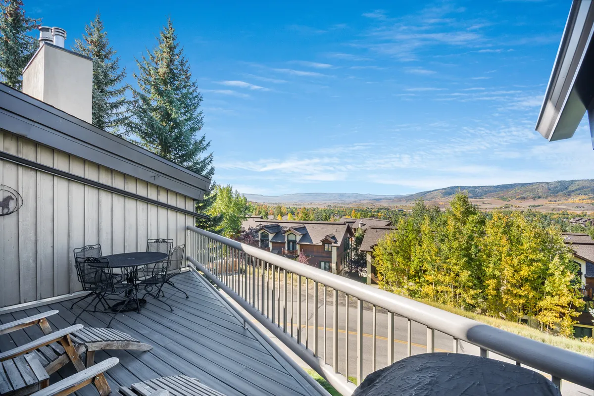 A scenic private balcony or deck adorned with comfortable outdoor furniture, offering sweeping views over the valley and surrounding trees. The tranquil setting is perfect for group breakfasts, evening relaxation, or simply soaking in the natural beauty of the Steamboat Springs area.