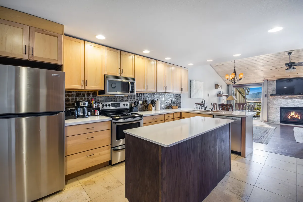 The image showcases an inviting kitchen with a central island, stainless steel appliances, and a cozy fireplace. The open space is ideal for cooking, entertaining, and sharing memorable moments with friends or a partner.