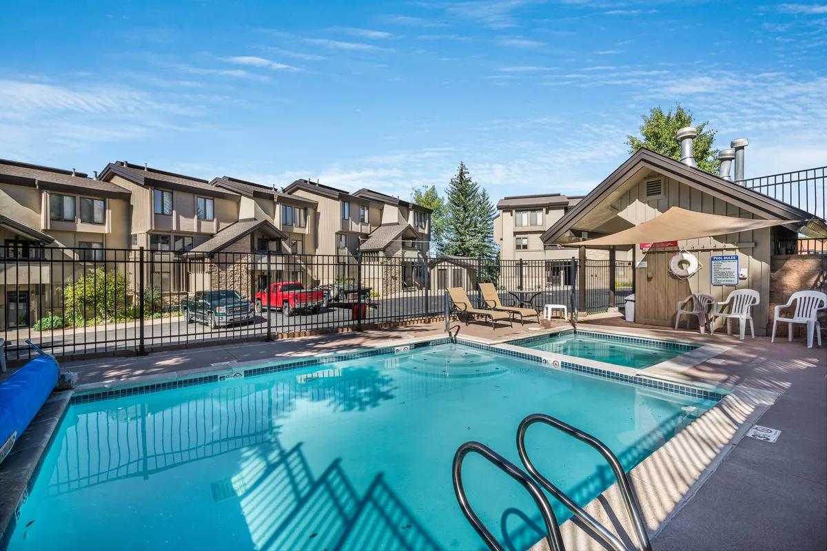 A lively exterior scene of the swimming pool area, featuring lounge chairs, a fenced perimeter, and surrounding buildings. The setting suggests opportunities for swimming, sunbathing, and gathering with friends or family, underscoring a relaxed resort atmosphere.