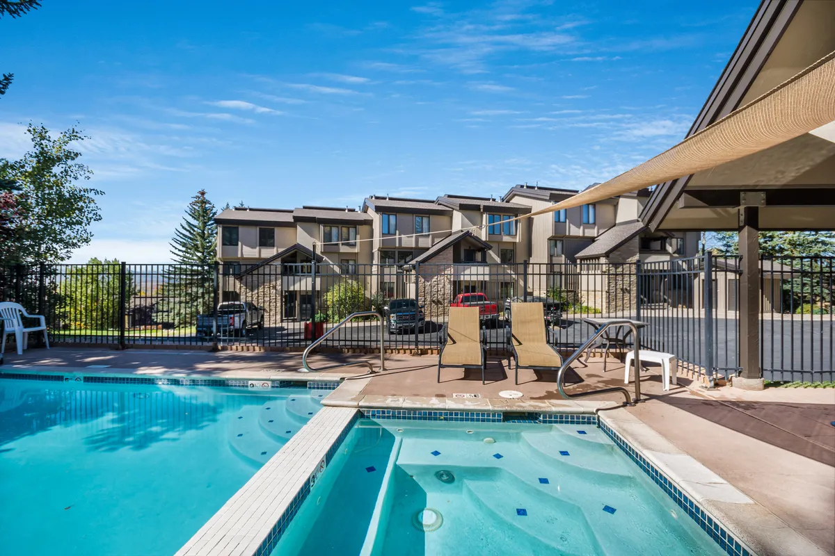 A tranquil outdoor scene featuring a sparkling swimming pool surrounded by lounge chairs and lush greenery, all enclosed within a safe fenced area. The setting captures a relaxed, fun atmosphere perfect for summer swimming, sunbathing, and social family time.